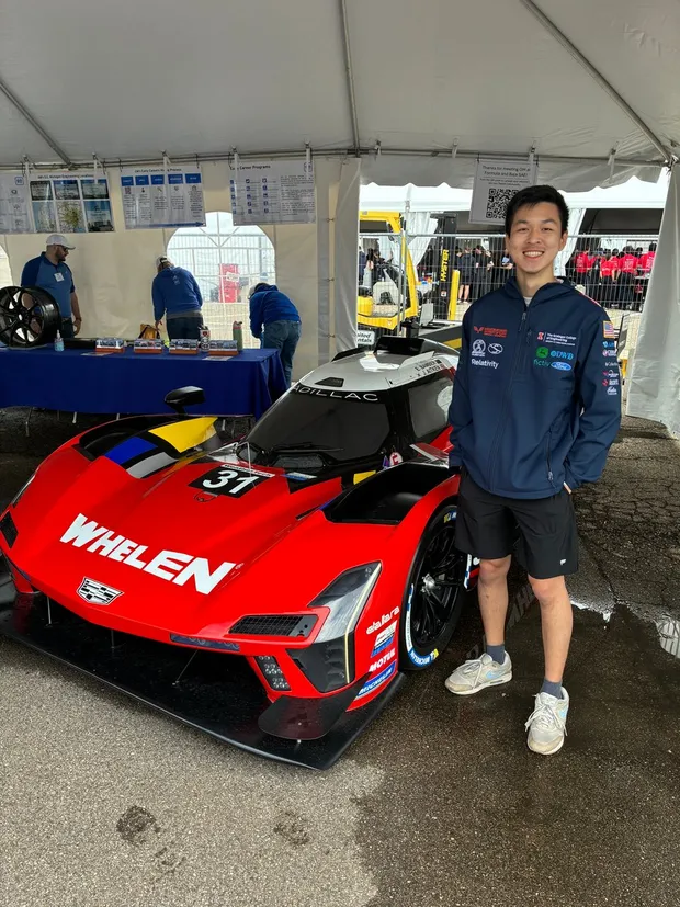 Charles Deng in a team jacket beside a race car at a Formula SAE event